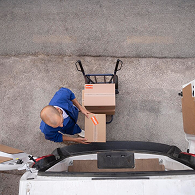 A mover in a green Xvanlines shirt stands on a green stepladder inside a moving truck, organizing "Lowe's" brand moving boxes and furniture wrapped in blue blankets and plastic.