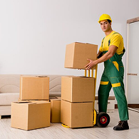 A mover in a green Xvanlines shirt stands on a green stepladder inside a moving truck, organizing "Lowe's" brand moving boxes and furniture wrapped in blue blankets and plastic.