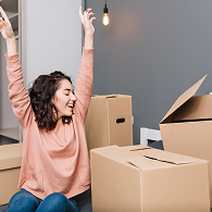 A mover in a green Xvanlines shirt stands on a green stepladder inside a moving truck, organizing "Lowe's" brand moving boxes and furniture wrapped in blue blankets and plastic.