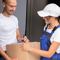 A mover in a green Xvanlines shirt stands on a green stepladder inside a moving truck, organizing "Lowe's" brand moving boxes and furniture wrapped in blue blankets and plastic.
