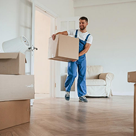 A mover in a green Xvanlines shirt stands on a green stepladder inside a moving truck, organizing "Lowe's" brand moving boxes and furniture wrapped in blue blankets and plastic.